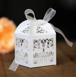 White laser-cut favor boxes with reindeer design and white organza ribbon on wood surface