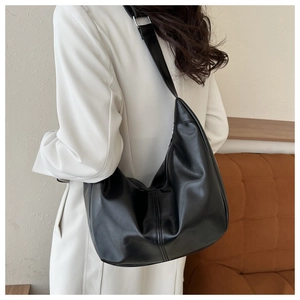 Detail view of the large black crescent shoulder bag on a model wearing a beige coat