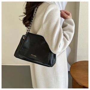 Détail du sac à bandoulière en cuir noir brillant avec chaîne dorée sur manteau blanc