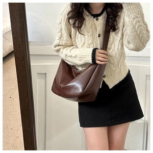 Detail of a large dark brown polished leather hobo bag worn with a casual outfit