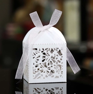 Detailed laser-cut pattern of white wedding candy box with a silk ribbon on a dark surface