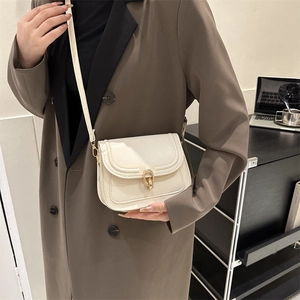 Sac bandoulière blanc cassé avec boucle dorée porté par un mannequin en manteau brun