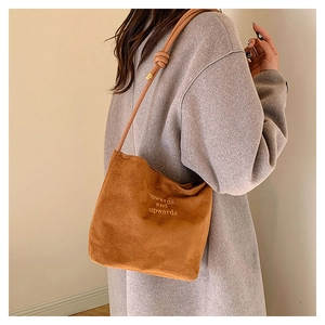 Détail d'un sac cabas en daim avec broderie texte et fine bandoulière en cuir souple