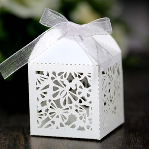 Macro detail of laser-cut white favor box with elegant butterfly pattern and silver ribbon