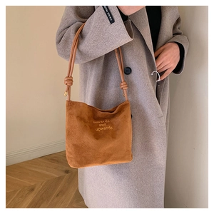 Détail du sac cabas en daim caramel avec broderie porté sur un long manteau gris