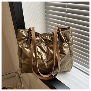 Détail d'un sac cabas matelassé doré métallisé avec texture rembourrée et anses brunes