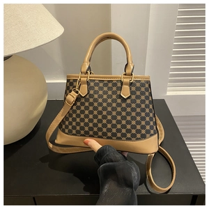 Close-up of trapezoidal handbag with black gold geometric pattern and beige leather handle