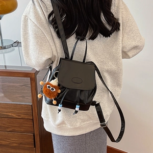Vintage college style black leather mini backpack with plush pendant worn by a model