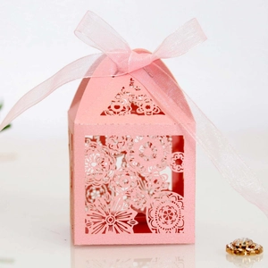 Detail of pink laser-cut wedding favor box with floral hollow patterns and ribbon