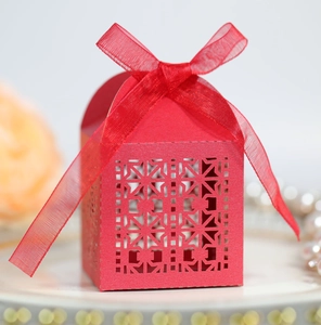 Close-up of red laser-cut wedding favor box with geometric patterns and red organza ribbon