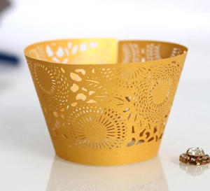 Golden laser-cut lace cupcake wrappers with intricate floral patterns on a white base
