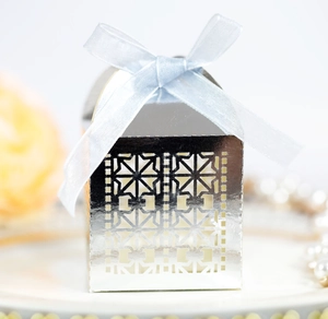 Close-up of silver laser-cut wedding favor box with light blue ribbon and pearl background