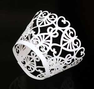 White laser-cut heart pattern cupcake wrapper with intricate lace design on black background