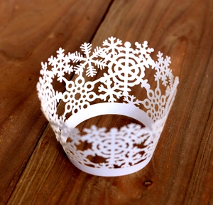 Detail of white laser-cut snowflake cupcake wrappers on a dark wooden surface