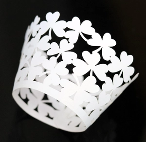 Detailed laser-cut white shamrock cupcake wrapper with intricate clover leaf patterns