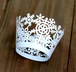 Detailed view of laser-cut white snowflake lace cupcake wrappers on a rustic wooden table