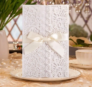 Detailed laser-cut lace invitation card with elegant cream satin ribbon bow on white china