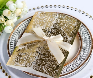 Detail of laser-cut gold wedding invitation with cream satin bow on decorative plate
