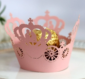 Pink laser-cut paper cupcake wrappers featuring crown and carriage designs for party decor