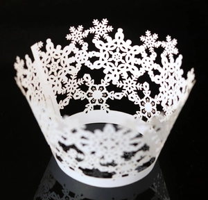 Macro detail of laser-cut white snowflake cupcake wrapper with delicate hollow pattern