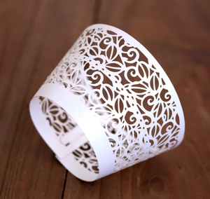 Elegant white laser-cut floral cupcake wrapper on a dark brown wooden surface