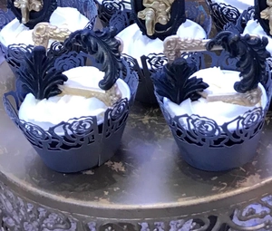 Detailed view of laser-cut black floral lace cupcake wrappers and gold party toppers