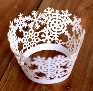 Detailed laser-cut white cupcake wrapper with snowflake patterns on wood background