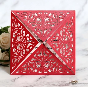 Close-up of red laser-cut wedding invitation with intricate scroll patterns on marble surface