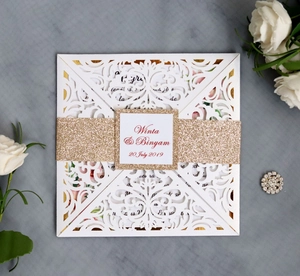 Detail of laser-cut white wedding invitation with gold glitter band and floral patterns