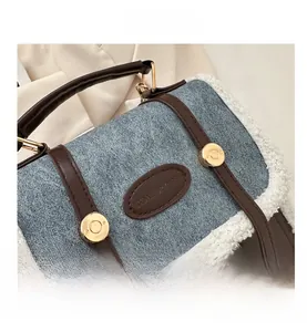 Detail of blue denim and white fleece trim bag with brown leather strap and gold hardware