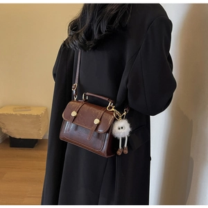 Detail of vintage brown textured leather handbag with plush monster charm and gold buckle