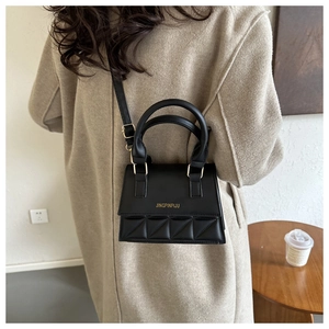 Detailed view of a black quilted leather handbag held by a model in a wool coat