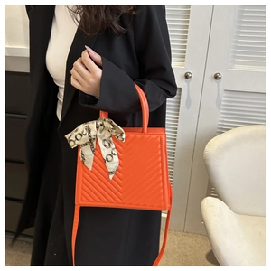 Détail d'un sac bandoulière matelassé orange avec foulard en soie décoratif sur l'anse