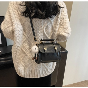 Detail of a black glossy leather crossbody bag with gold buckles and a white plush charm