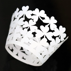 Intricate laser-cut four-leaf clover cupcake wrapper in white cardstock for wedding decor
