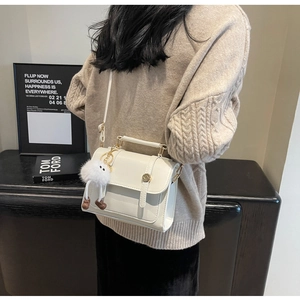 Detail of minimalist cream square shoulder bag featuring a cute plush pendant and gold clasp