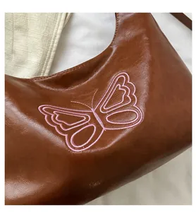 Close-up of pink butterfly embroidery on a dark brown vintage textured leather tote bag