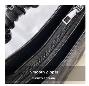 Detail of smooth metal zipper and ruffled leather strap on this black pleated handbag