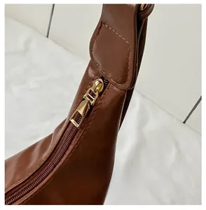 Detail of the smooth golden metal zipper closure on a brown soft leather tote bag