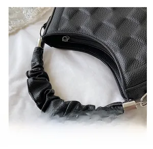 Close-up of a black lychee texture handbag with a unique scrunchie style handle and silver zipper