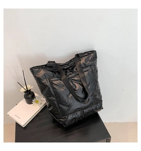 Close-up of a black quilted down fabric tote bag with a metallic finish on a black table