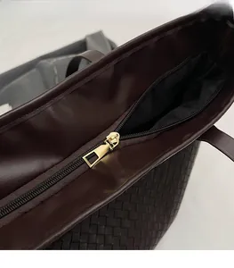 Detail view of smooth gold zipper and woven dark brown leather texture on a tote bag