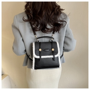 Detail of a black PU leather backpack with white faux shearling trim on a grey blazer