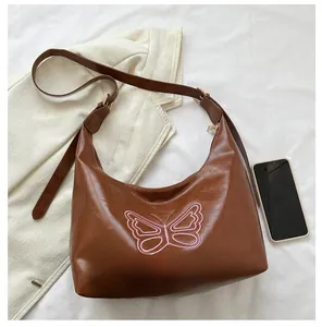Brown leather hobo bag with pink butterfly embroidery next to a phone for size