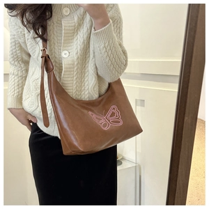 Close-up of brown leather hobo bag with pink embroidered butterfly and adjustable strap