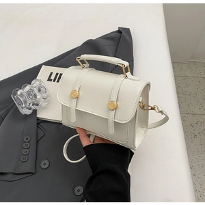 Detail of a beige mini faux leather handbag featuring a gold rotary clasp and top handle