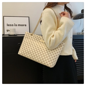 Detail of a large cream tote bag with brown geometric patterns and gold chain straps