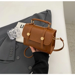 Detail of a brown vintage square handbag with matte leather texture and metal buckles