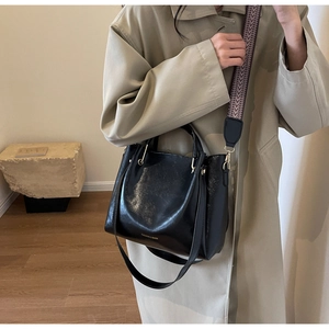 Dettaglio della borsa in pelle verniciata nera con tracolla larga a fantasia e oro