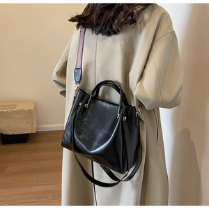 Borsa tote nera lucida con tracolla larga a motivi su modella in trench color kaki